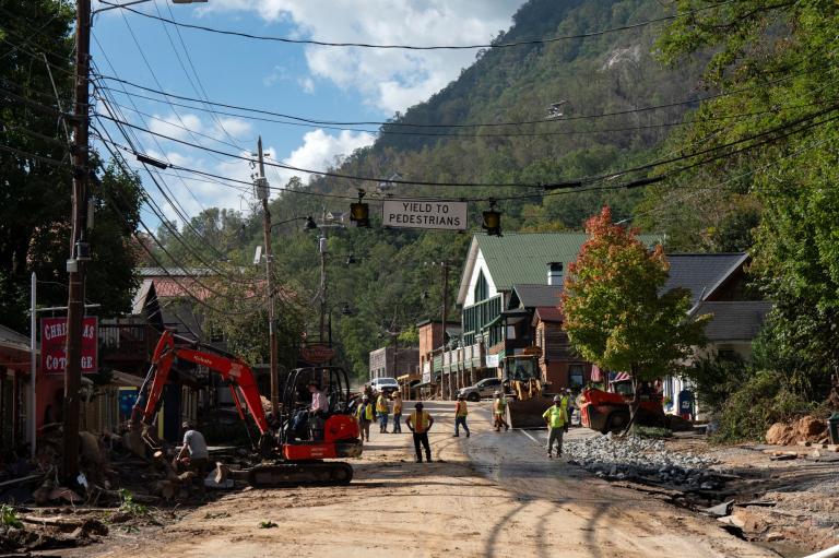 A photo looking down a muddy street, with construction equipment along the sides and workers in high-vis vests looking on.