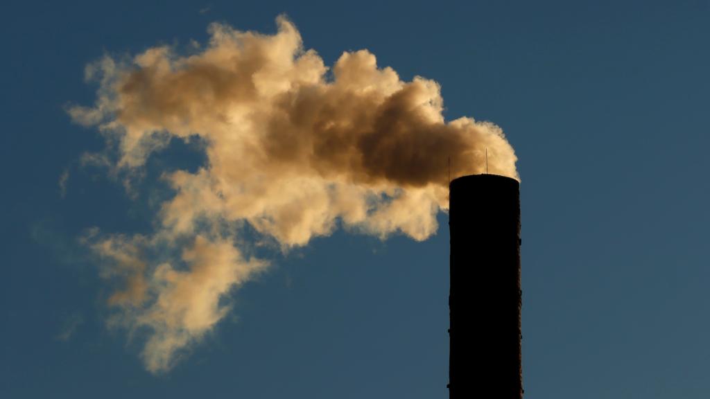 A smokestack spews emissions against a blue sky