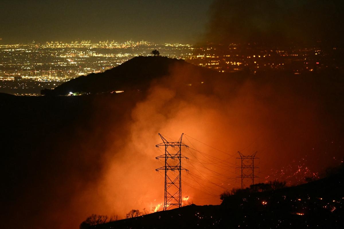 A fire rages at night with a transmission line in the foreground