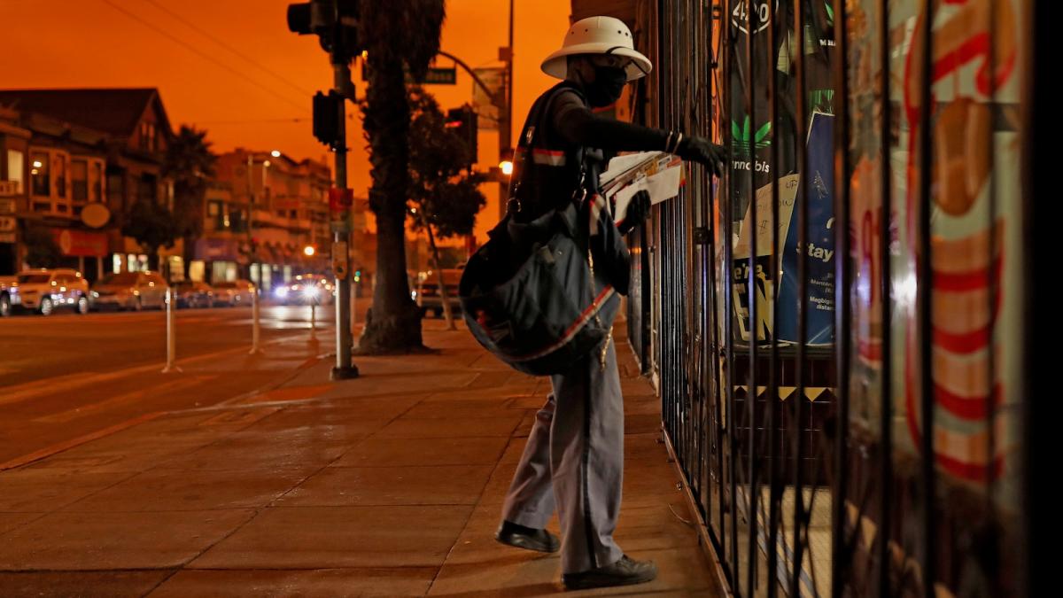 A postal carrier makes deliveries in San Francisco, the mid-day sky darkened and orange from smoke wafting in from wildfires burning hundres of miles away.