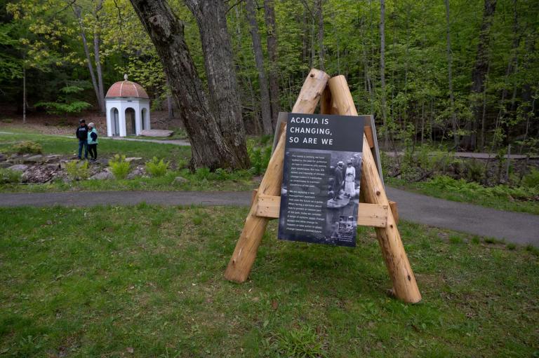 a national park sign on an a-frame stand reads 'acadia is changing, so are we'