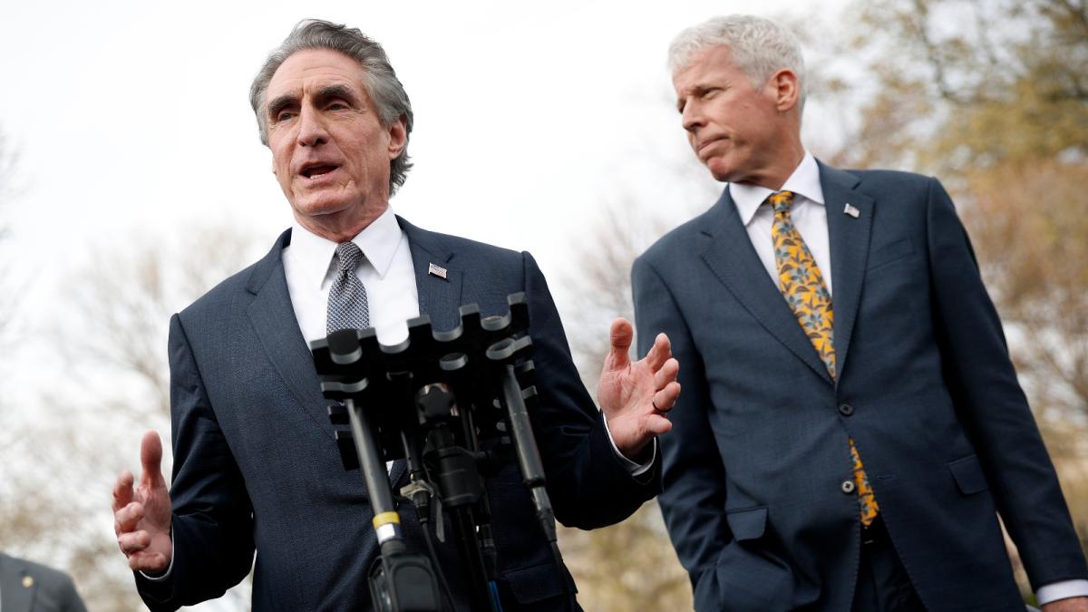 Two men in suits stand in front of a microphone