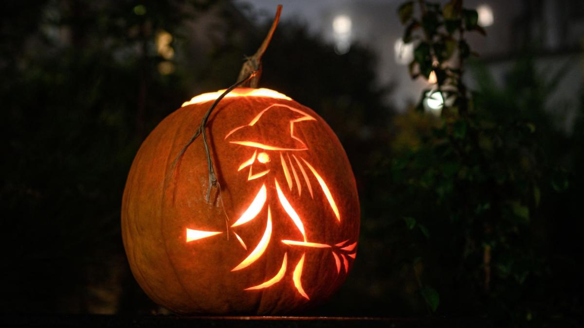 A photo of a glowing pumpkin carved with an image of a witch riding a broomstick