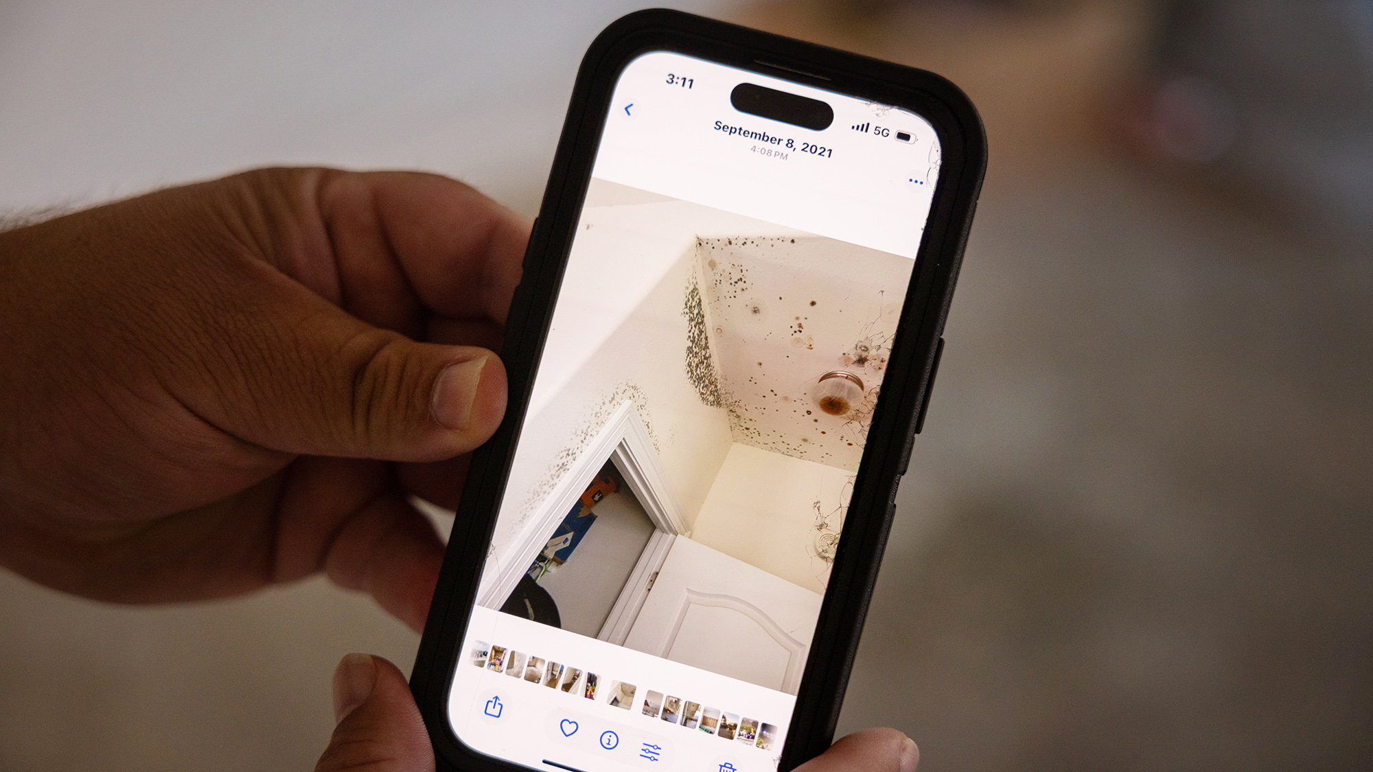 a man's hands hold a smart phone showing damaged and mold-ridden house ceilings with a date of September 8, 2021