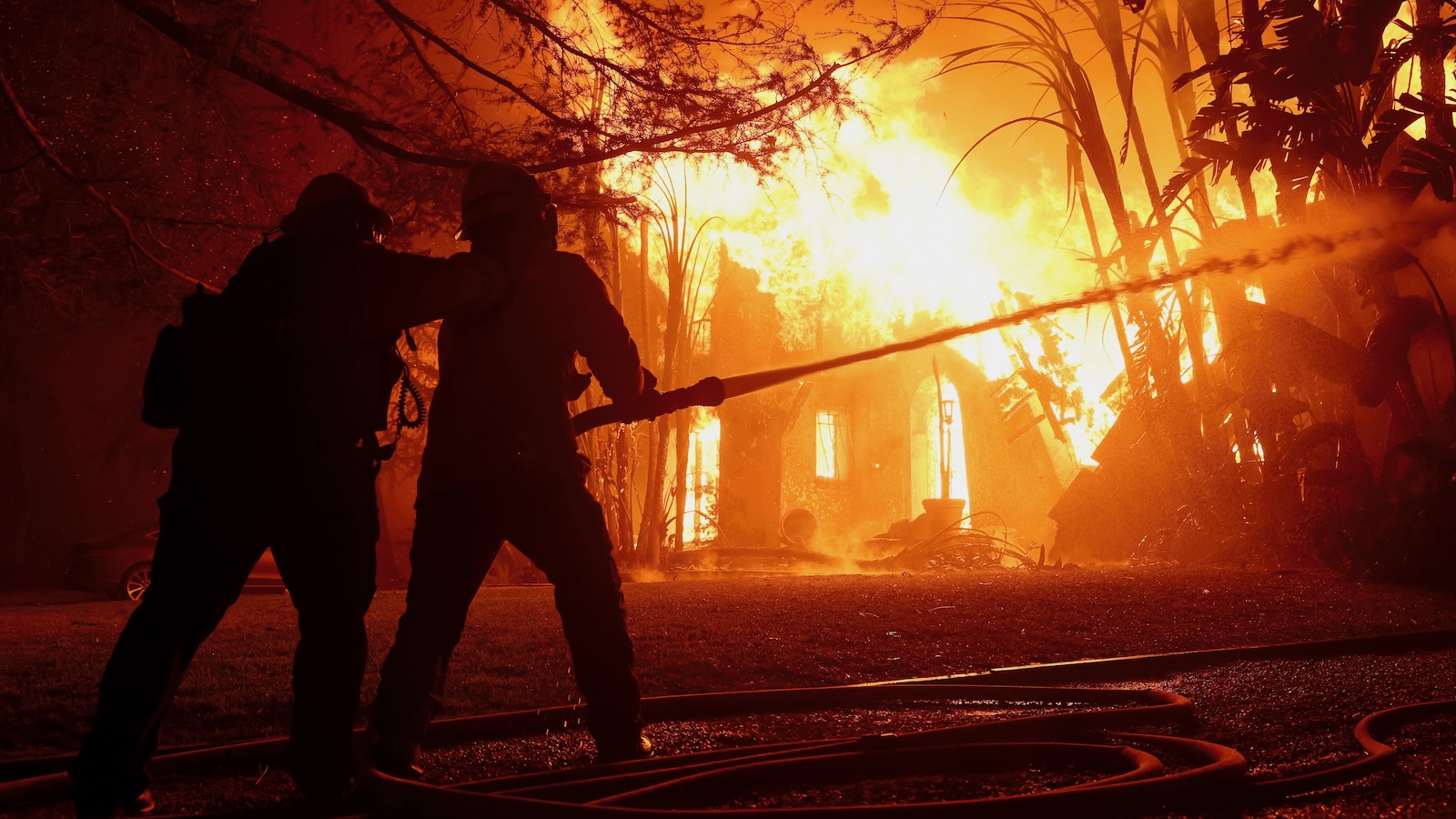 Two firefighters are seen silhouetted against the flames of a burning house in Altadena, California.