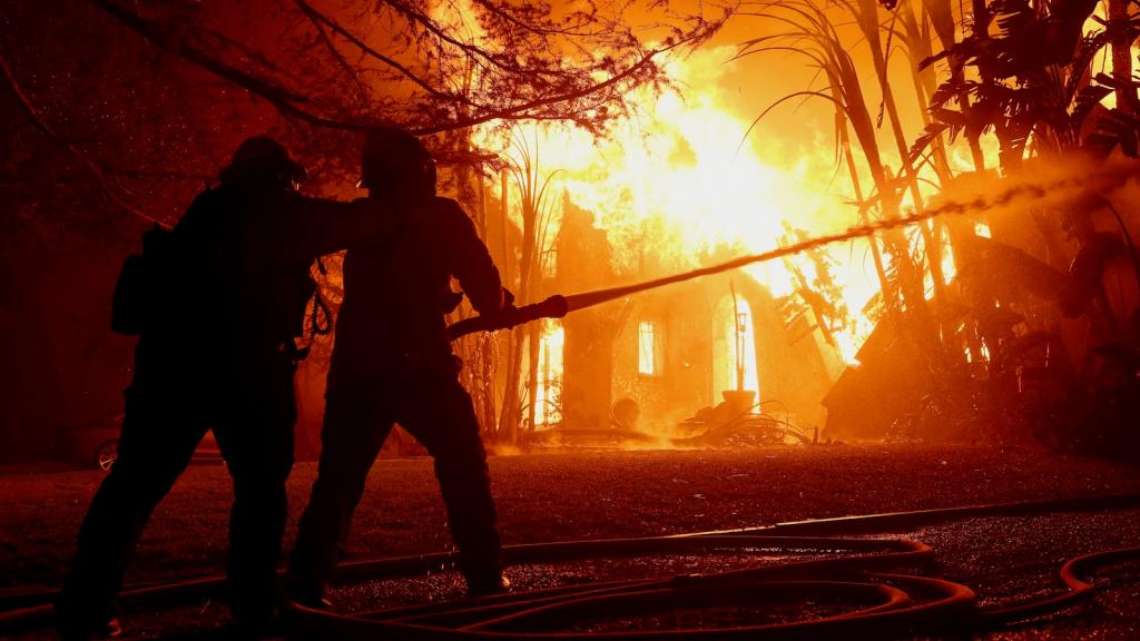 Two firefighters are seen silhouetted against the flames of a burning house in Altadena, California.
