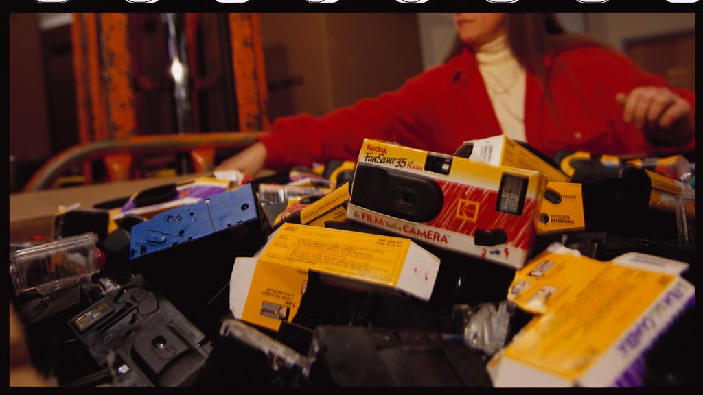 close up of disposable cameras in a pile with a woman in the background