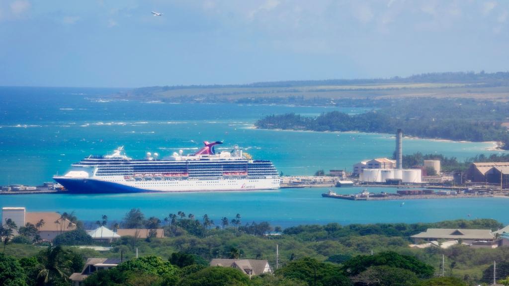 A huge white cruise ship sits in turquoise blue waters off the shore