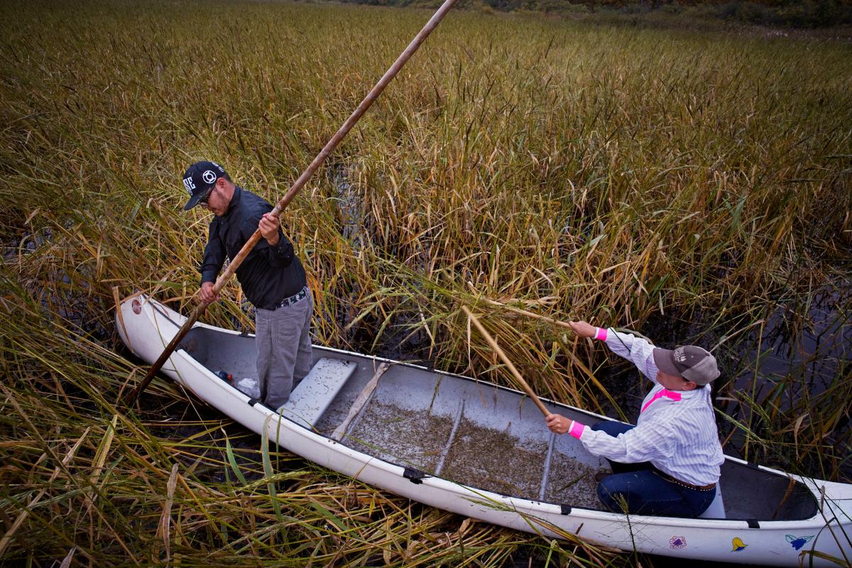 Two people on a canoe holding a long stick