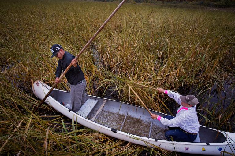 Two people on a canoe holding a long stick