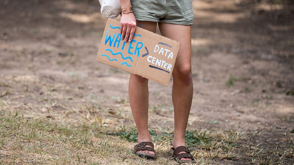 Lower half of a woman carrying a sign that reads water > data centers