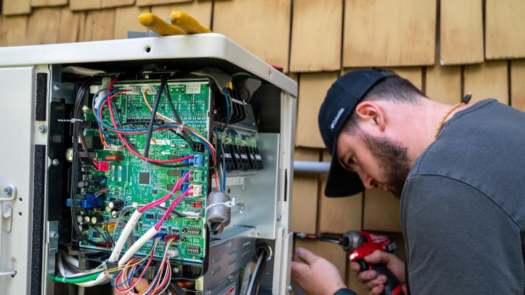 A man in a baseball cap uses tools on an electrical panel