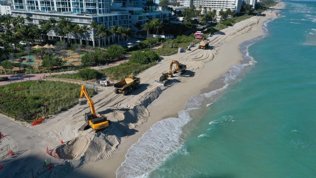 Photo of construction work to add sand to a beach with palm trees and buildings