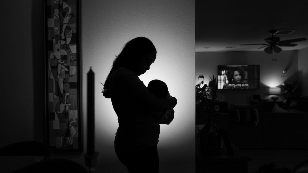 A woman stands in silhouette while holding a baby