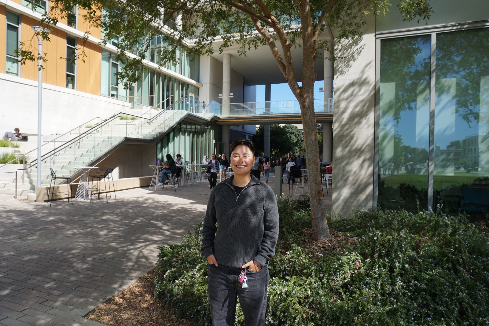 A young woman in pants and a sweatshirt stands in front of a building