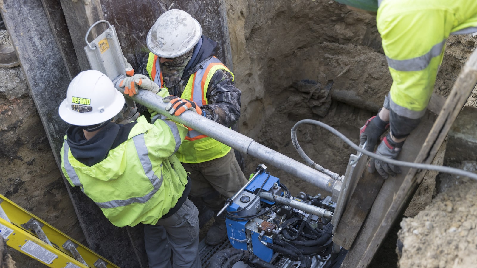 Three plumbers in green jackets installing a new water service line.