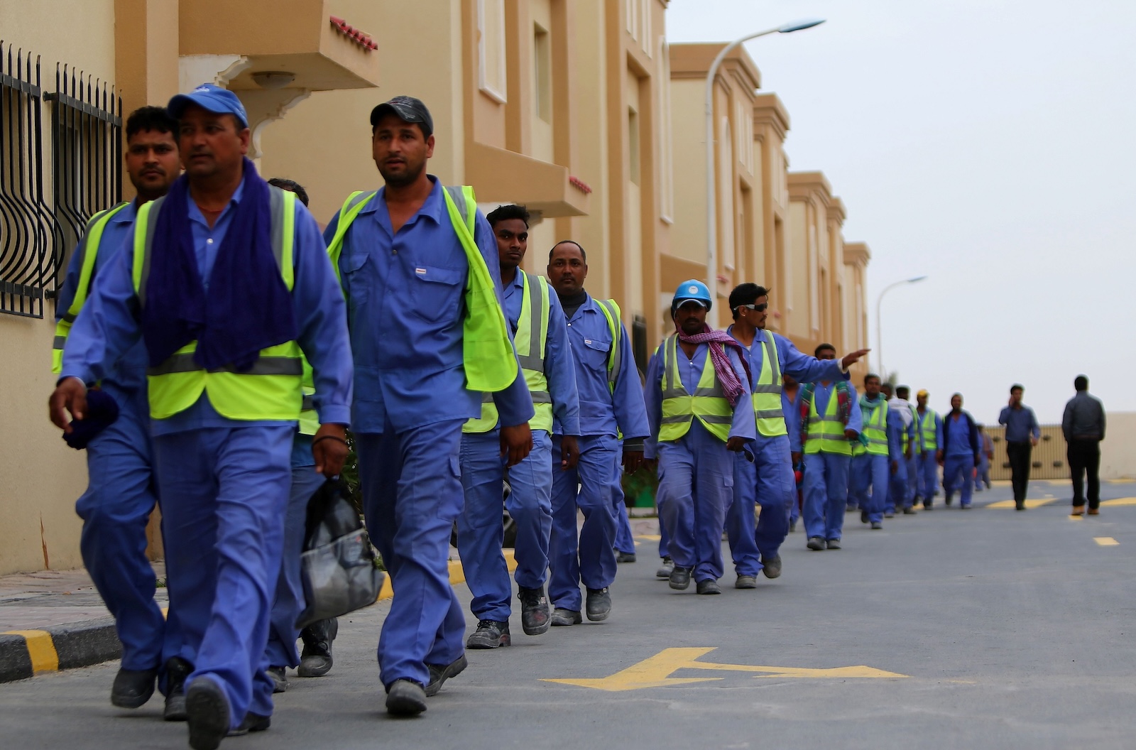 a group of men in construction uniforms walk in a line near buildings