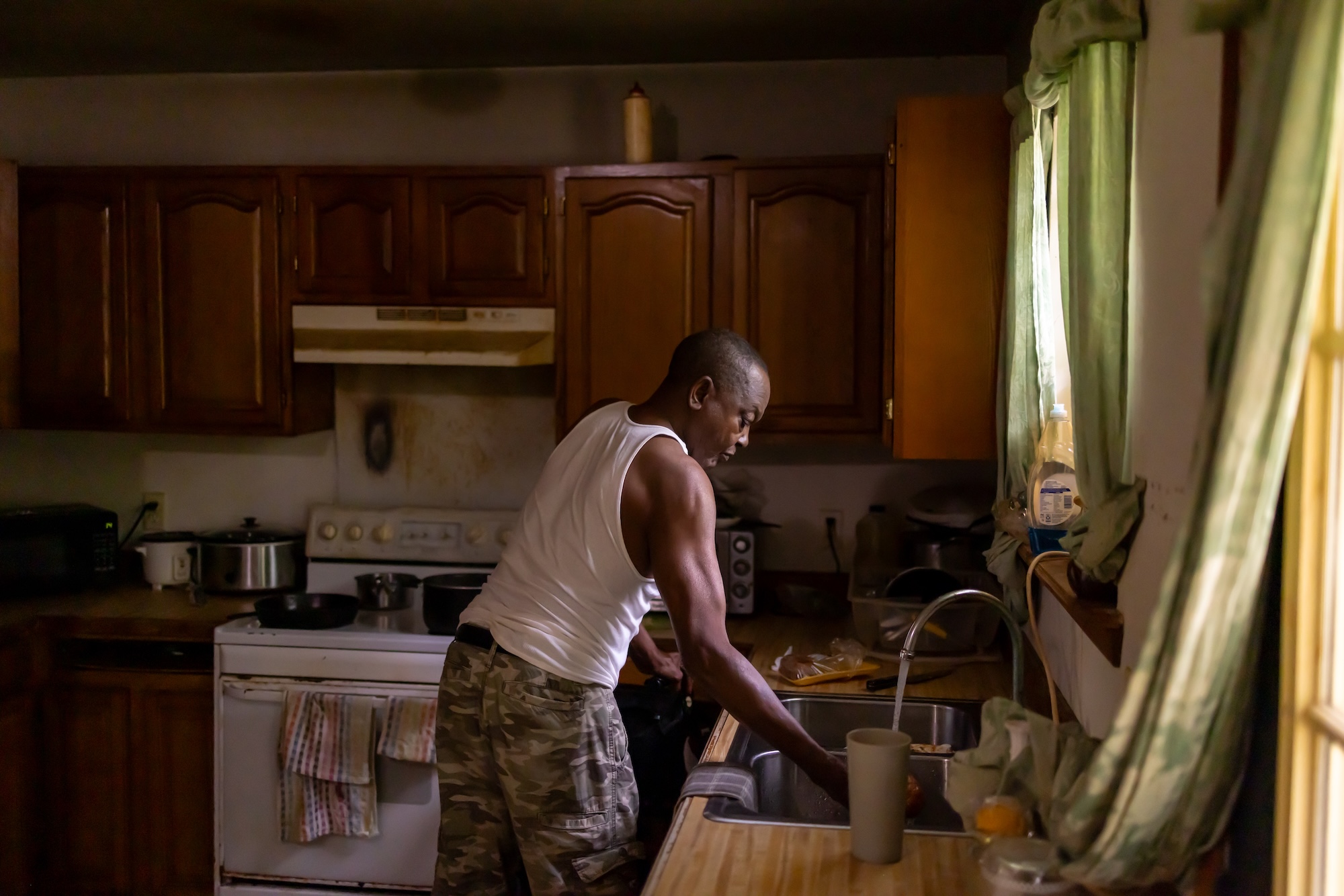 A man in his kitchen leans over the sink