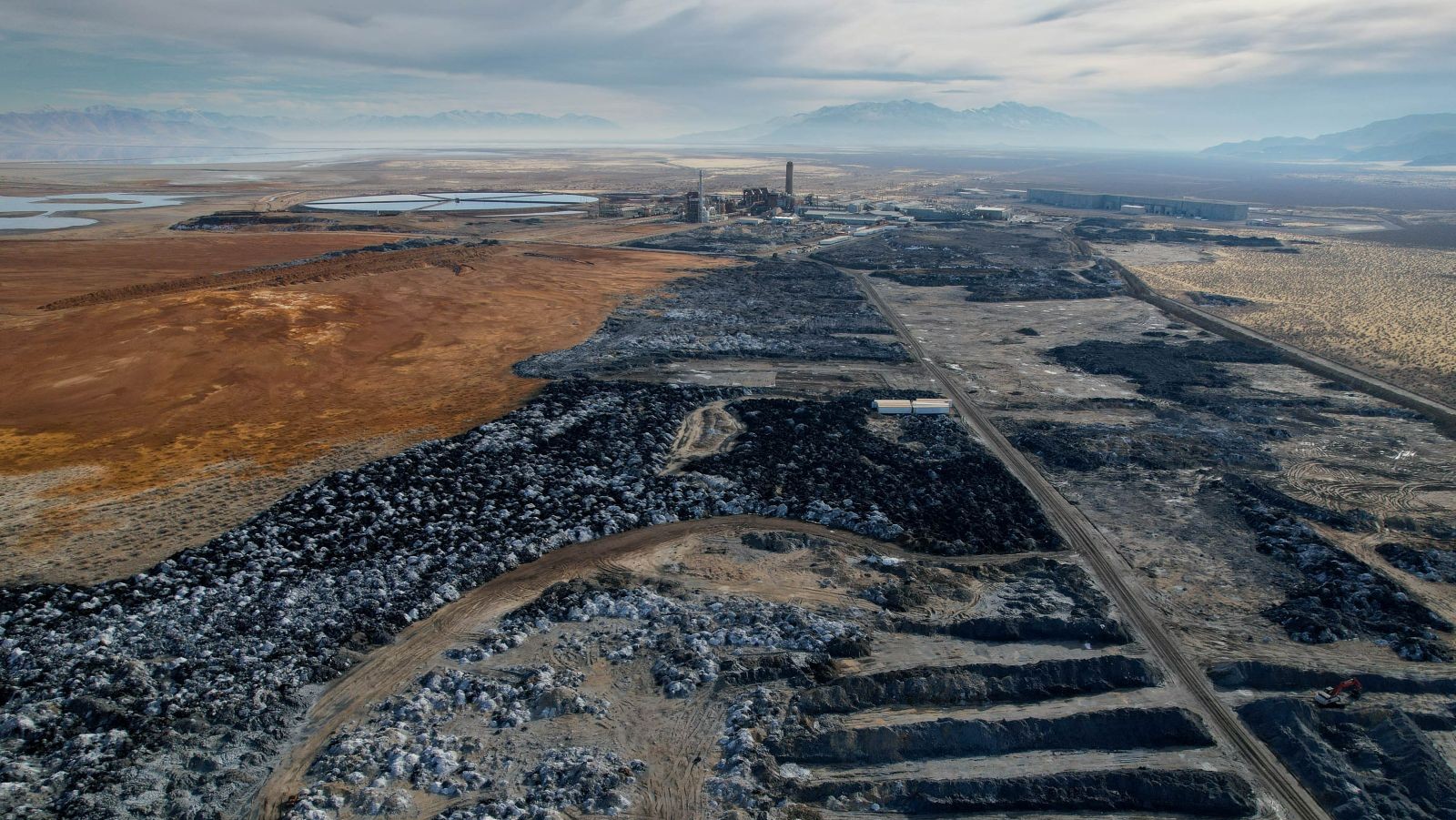 A large industrial site with rocky waste piles and mountains in the background.