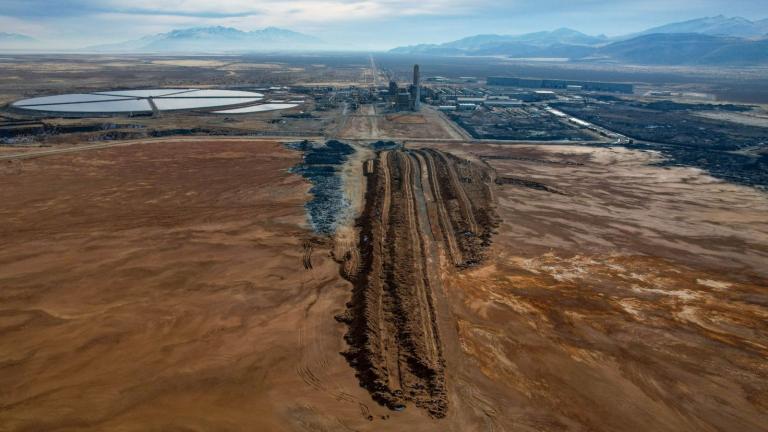 A sprawling industrial site with a large, unfinished barrier wall trenched into a lake playa