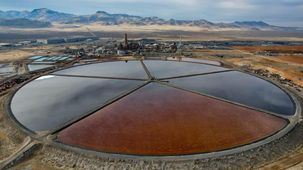 An industrial site with a circular waste pond and mountains in the background.