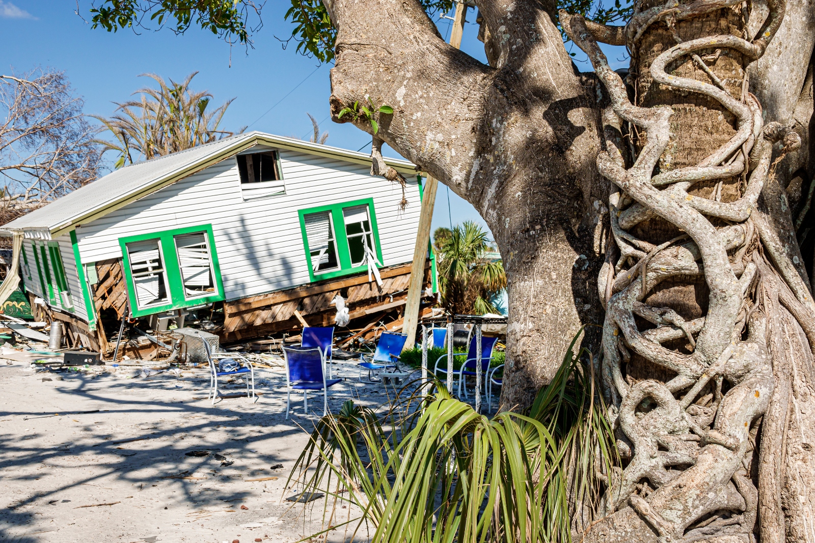 A damaged house slumps over on a sandy yard