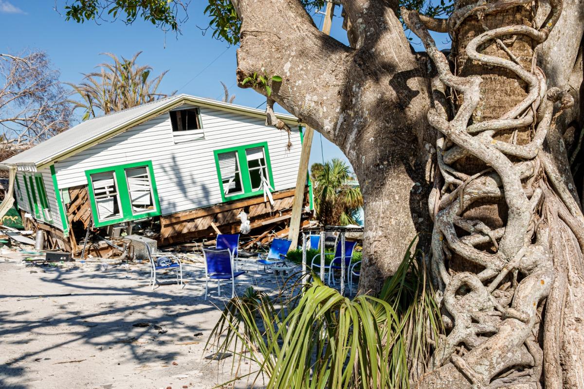 A damaged house slumps over on a sandy yard