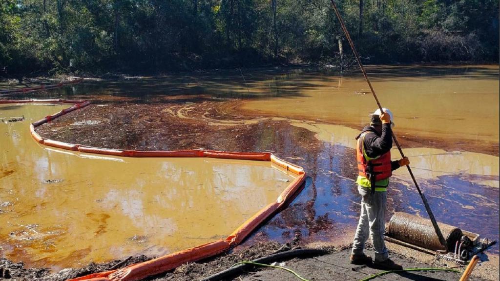 A man stands on the edge of a river filled with coffee colored sludge