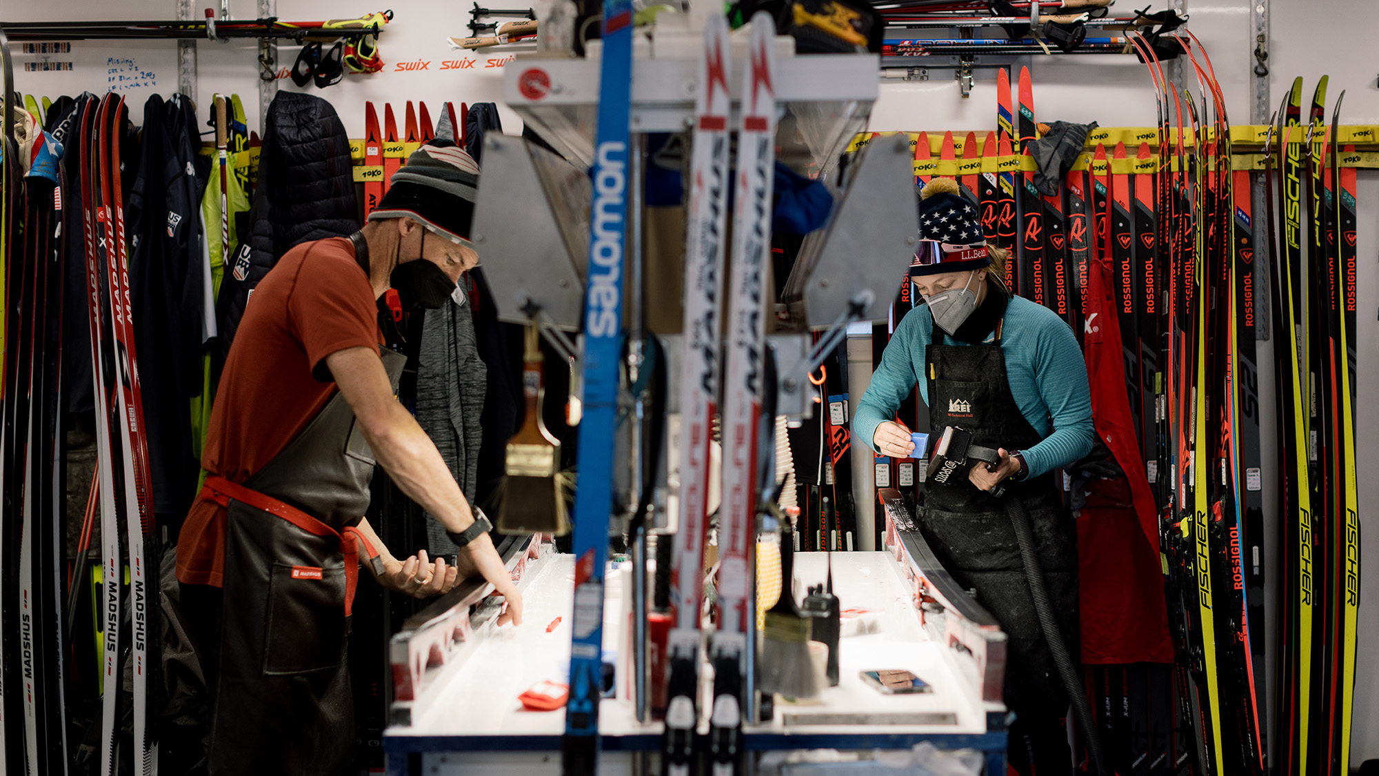 Two people apply wax to skis in a small room