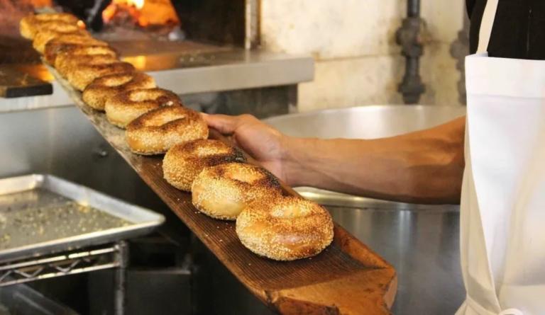 A row of fresh bagels coming out of a commercial oven