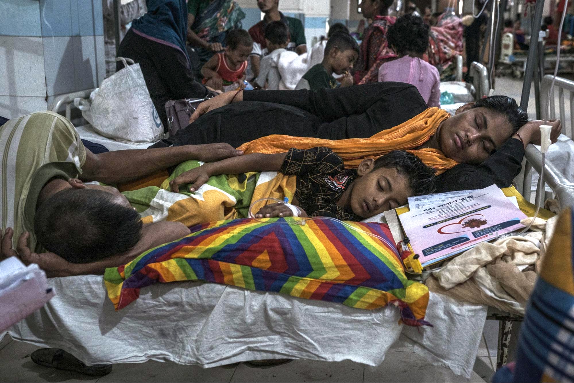 A woman and man lie near a child on a cot in a hospital