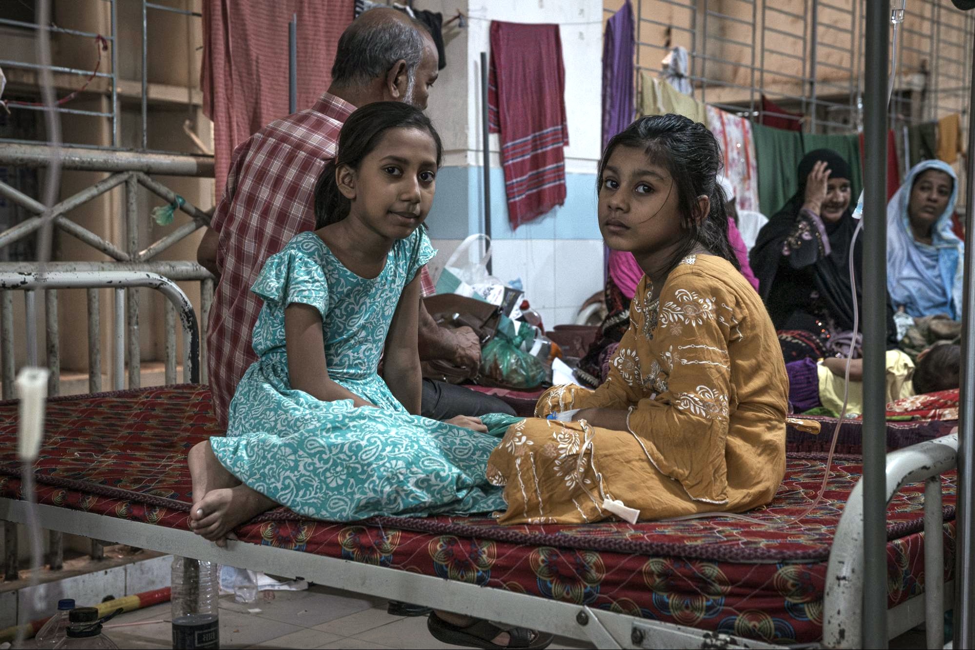 two young girls sit on a cot in a hospital setting in Bangladesh