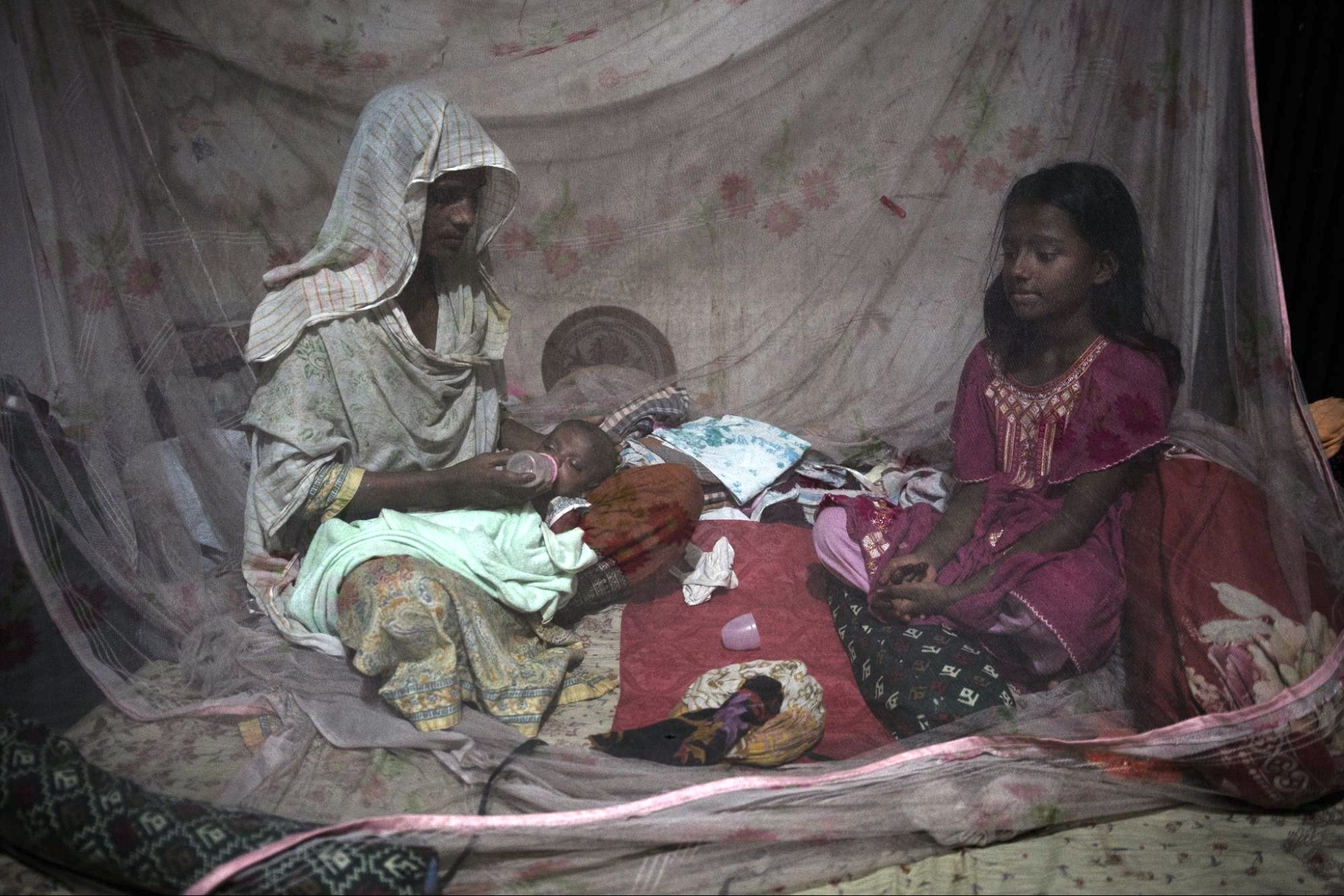 a woman sits with a young girl and a baby under a mosquito net