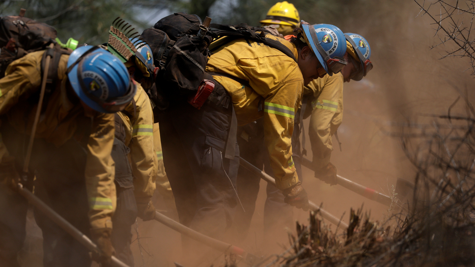 Photo of people in yellow jackets and hard-hats working with shovels in smoky conditions