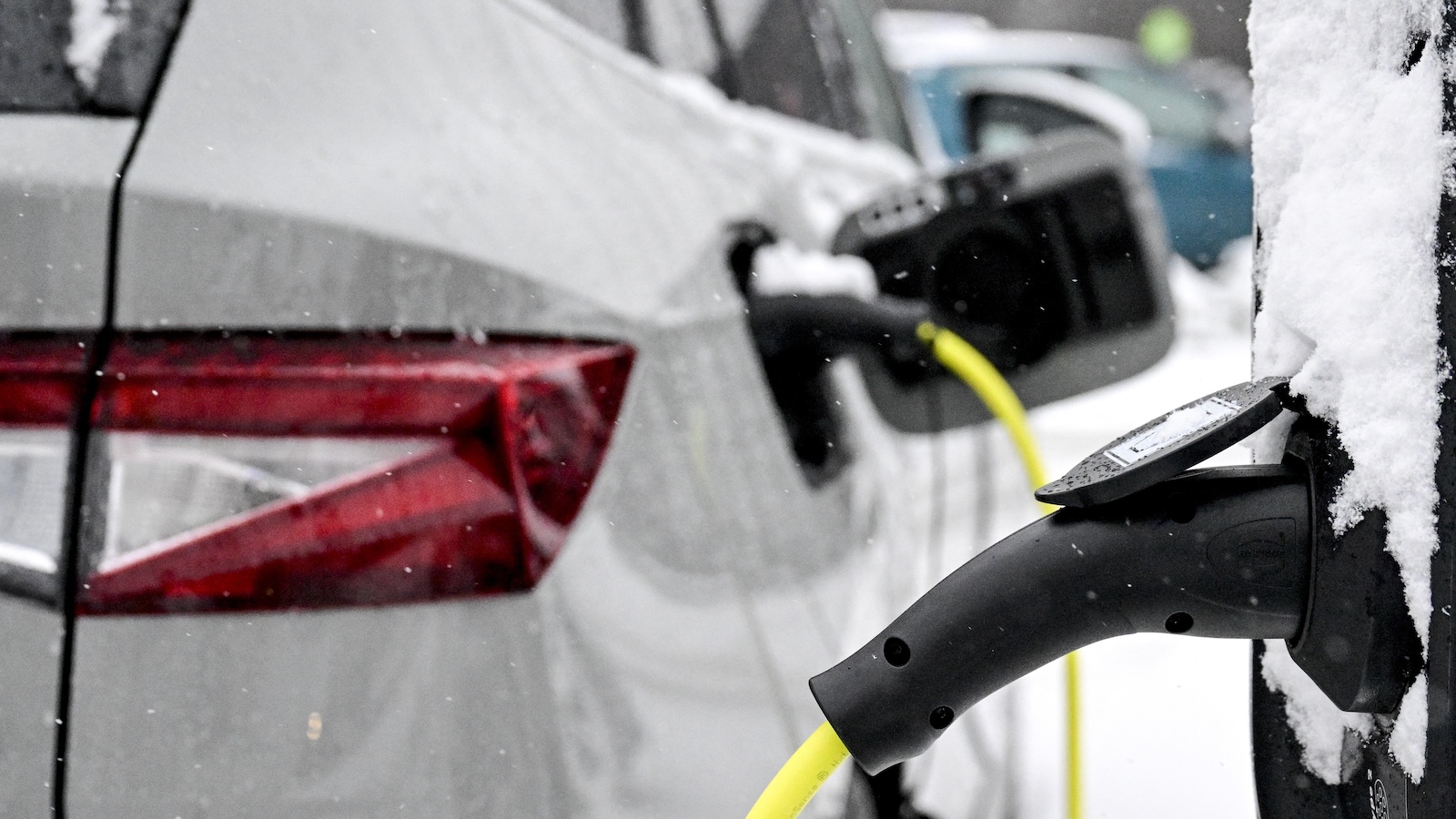 An electric vehicle covered in snow is shown plugged into a charger.