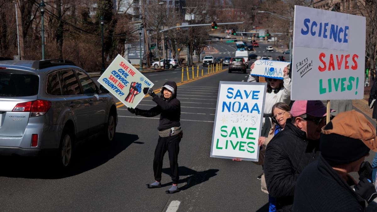 People protest along the side of the road with signs showing "save NOAA save lives"