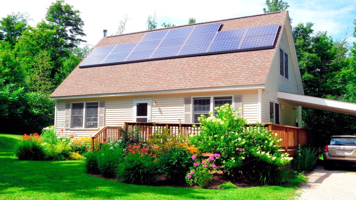 A brown and white house sits on a bright green lawn with solar panels on the roof