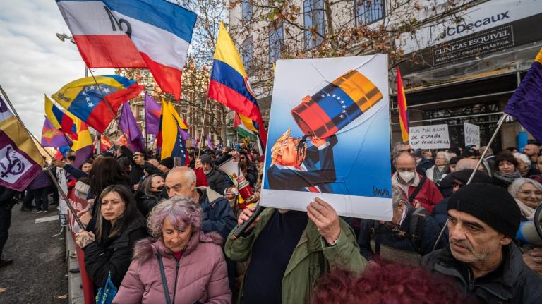 A man holds a placard showing President Donald Trump drinking from a barrel of oil during a protest outside the American embassy in Madrid. Trump has justified his abduction of Venezuelan leader Nicolás Maduro by claiming the United States will help tap Venezuela's oil reserves.