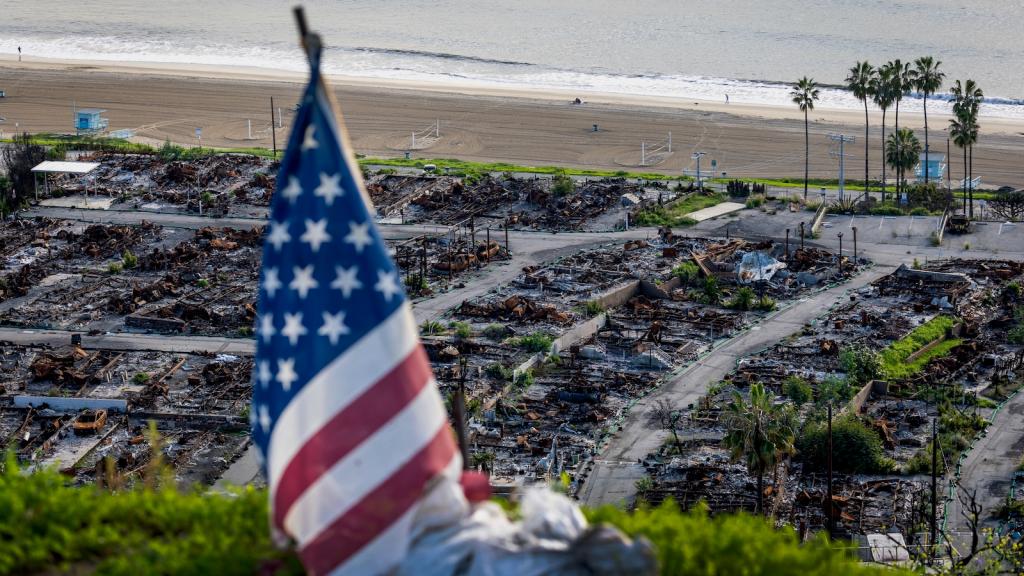 An American flag stands on a cliff overlooking a Pacific Palisades neighborhood one year after the fires that ravaged Los Angeles.