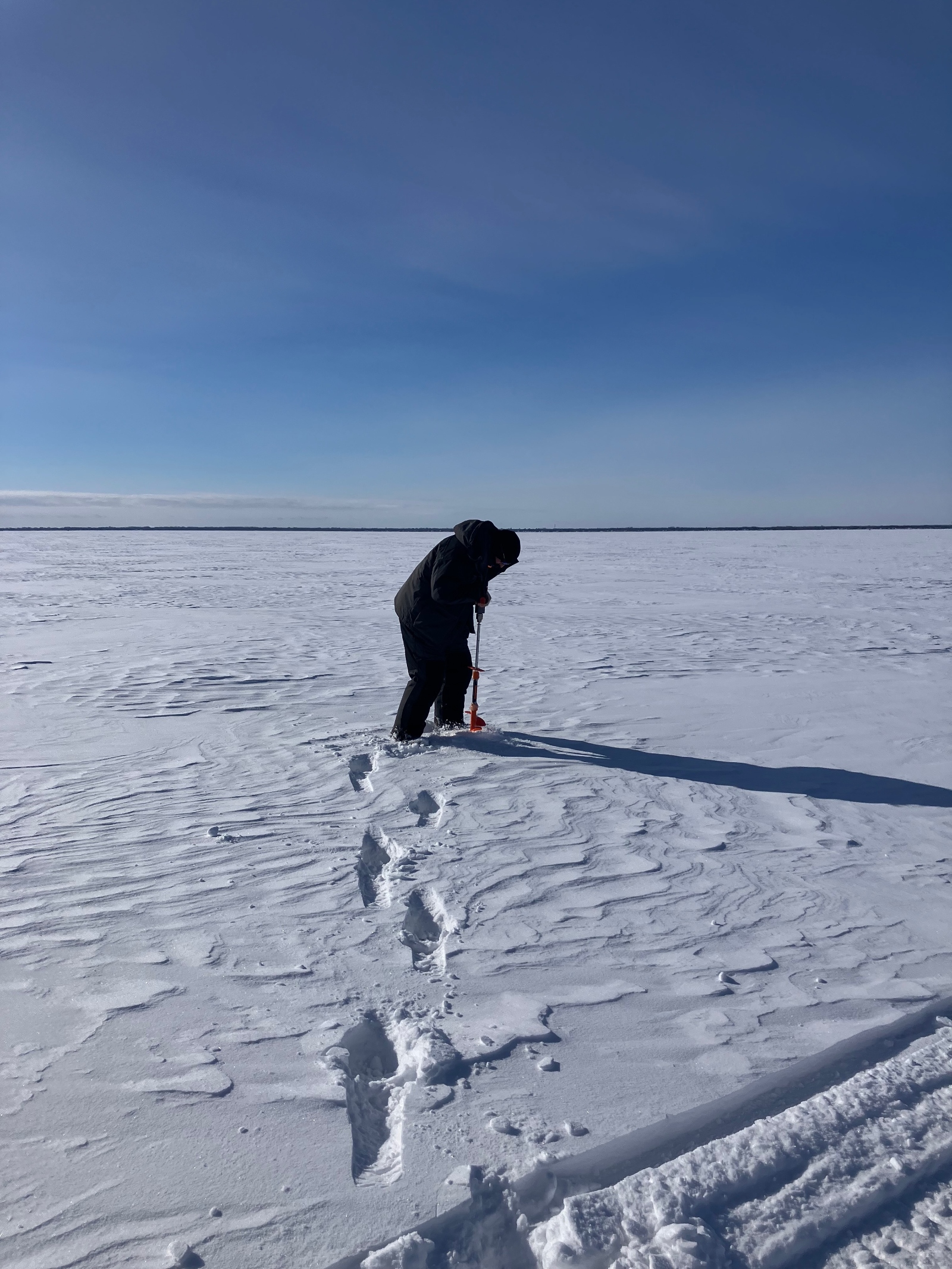 A man uses an auger to drill into ice