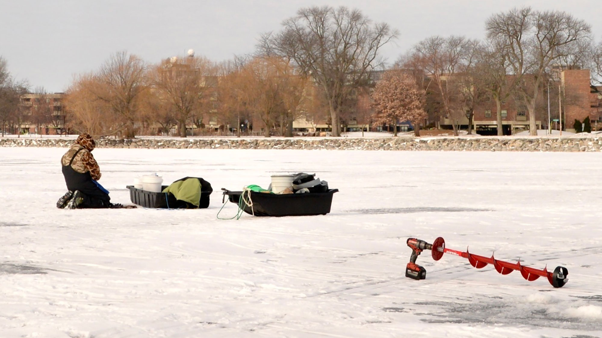 person in winter gear on frozen lake measuring the thickness of the ice