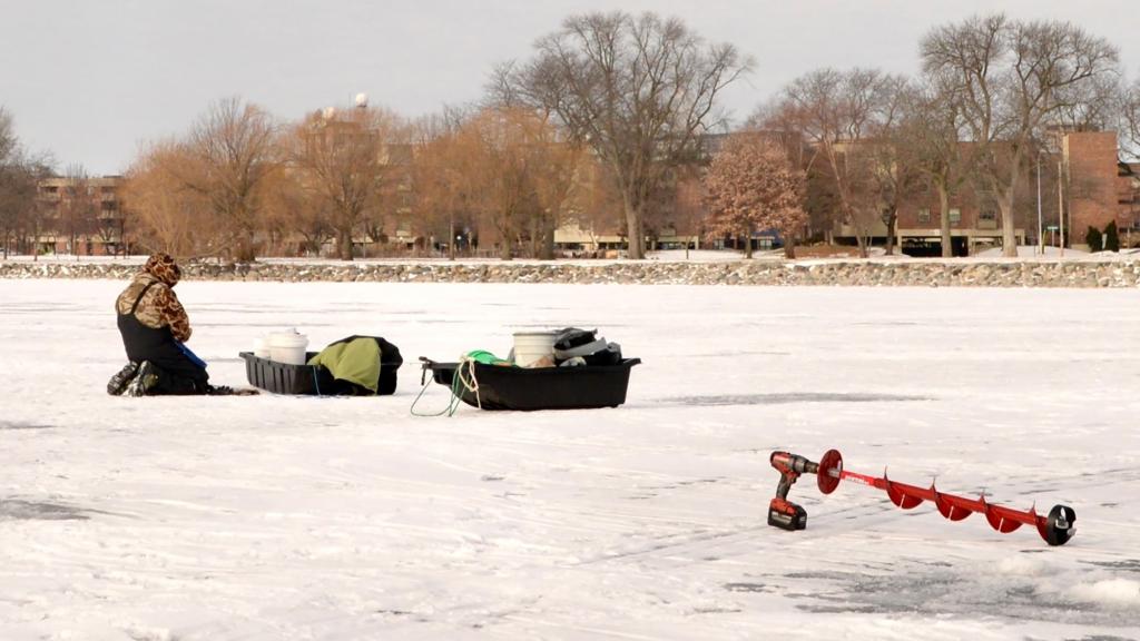person in winter gear on frozen lake measuring the thickness of the ice