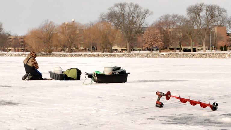 person in winter gear on frozen lake measuring the thickness of the ice