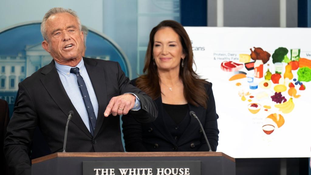 Health secretary Robert F Kennedy, Jr. stands behind a White House branded podium, behind him to the right stands agricultural secretary Brooke Rollins and a large posterboard showing the new inverted food pyramid