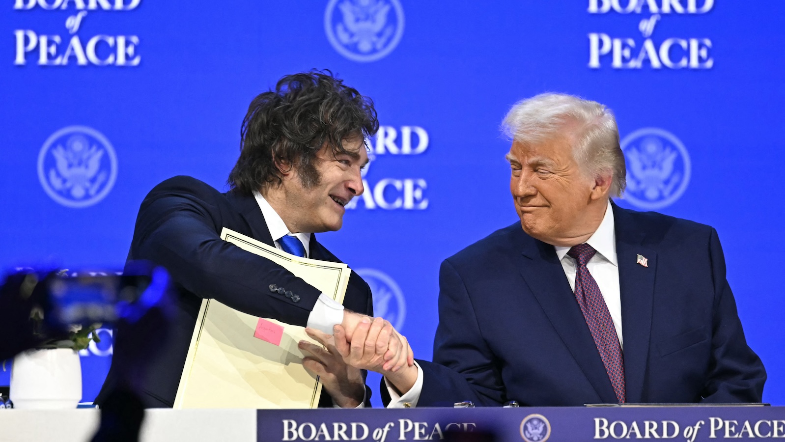 US president Donald Trump and Argentina president Javier Milei shake hands at the World Economic Forum while seated at a table against a blue backdrop