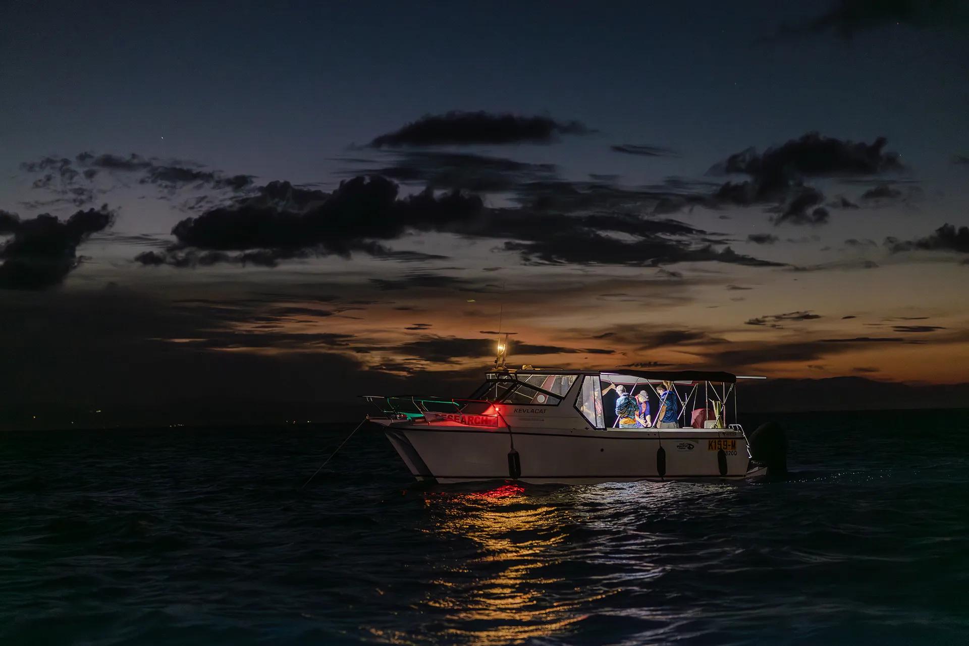 The sun dips on the horizon as a boat sits on the water in the dark