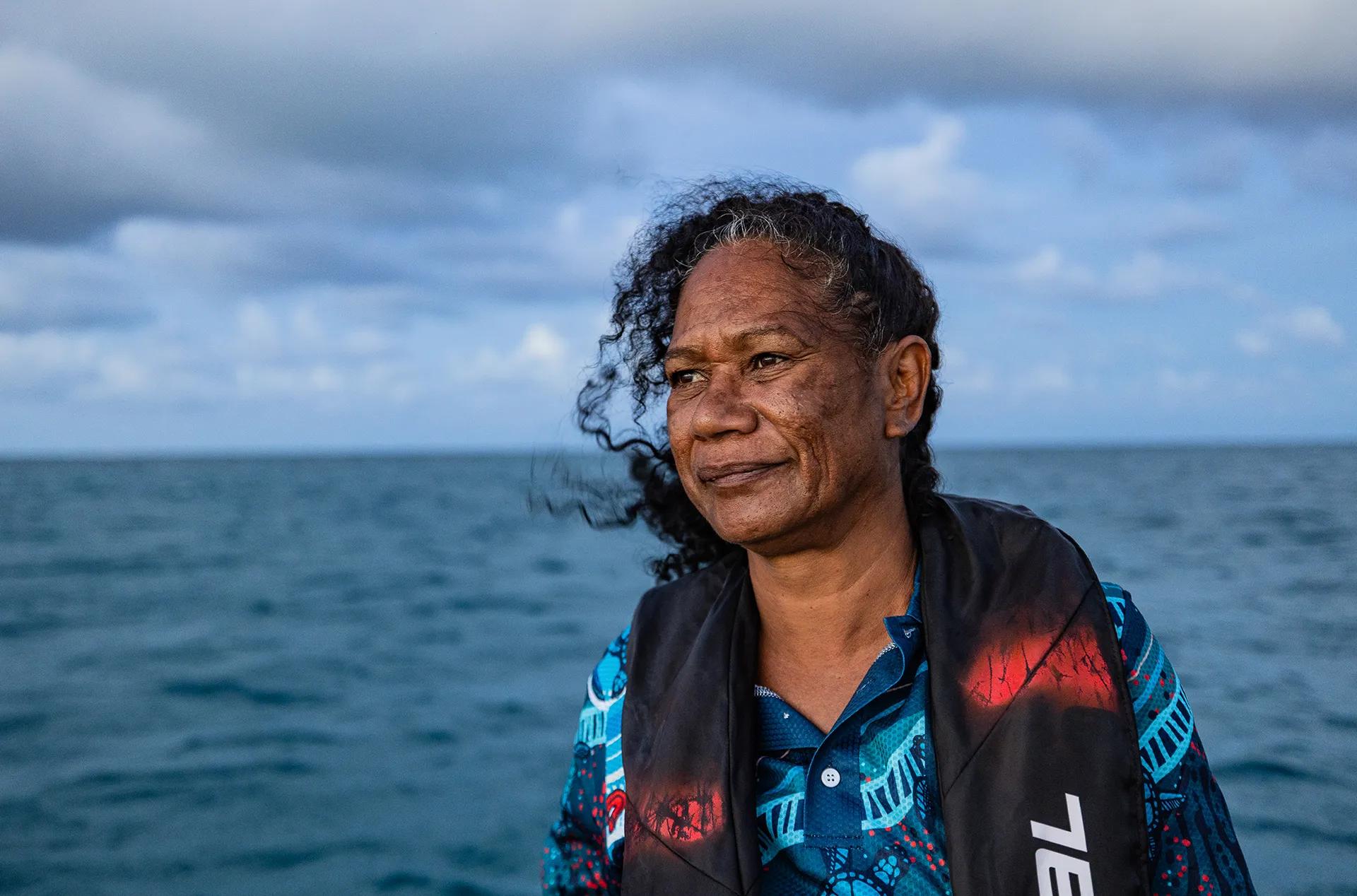 A woman in a colorful shirt stares into the horizon over the ocean