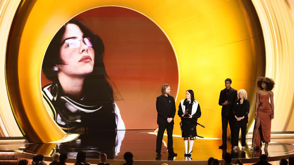 Finneas and Billie Eilish on stage with 3 other people at the Grammys