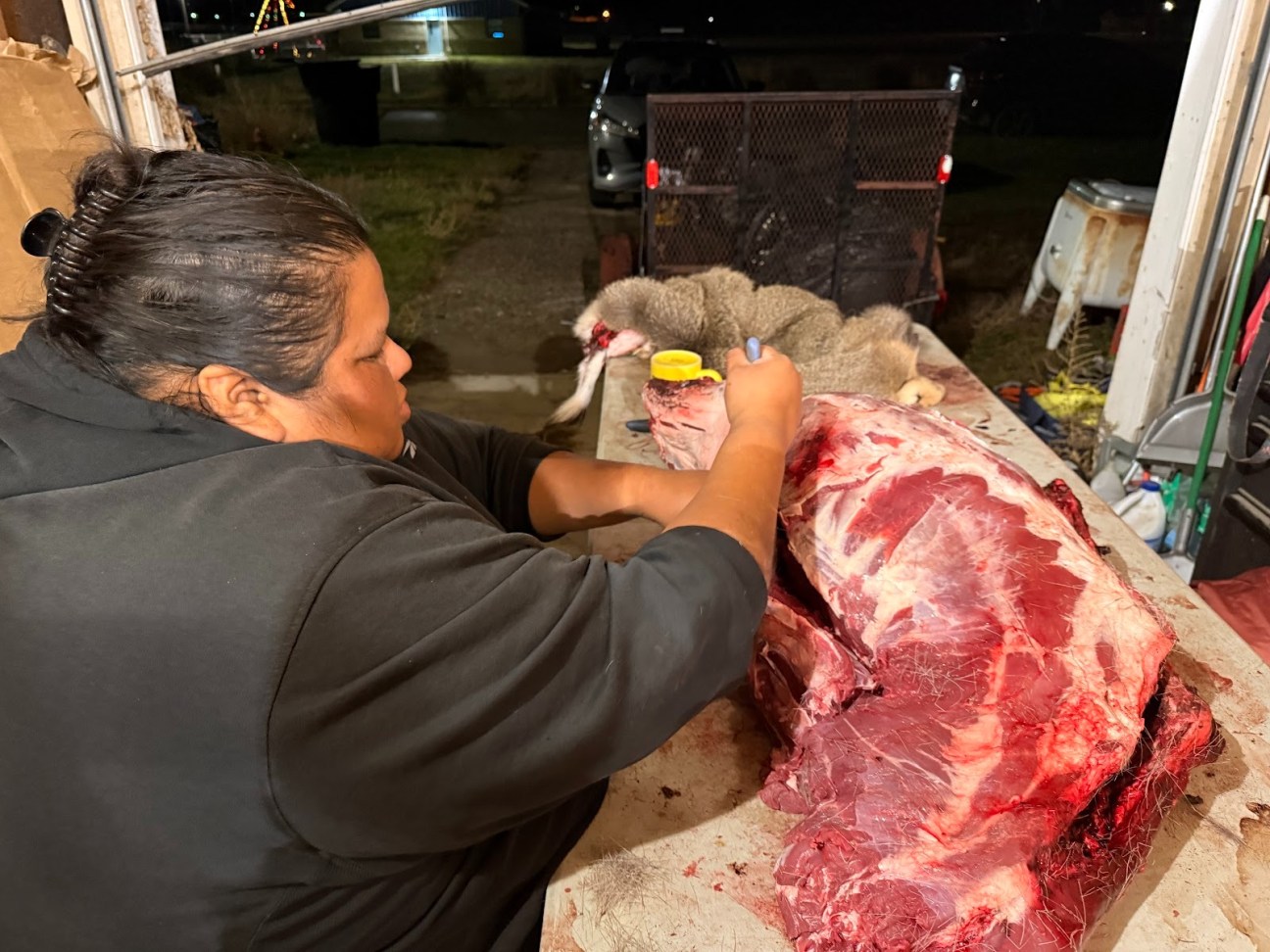 A woman carves dear meat in a garage