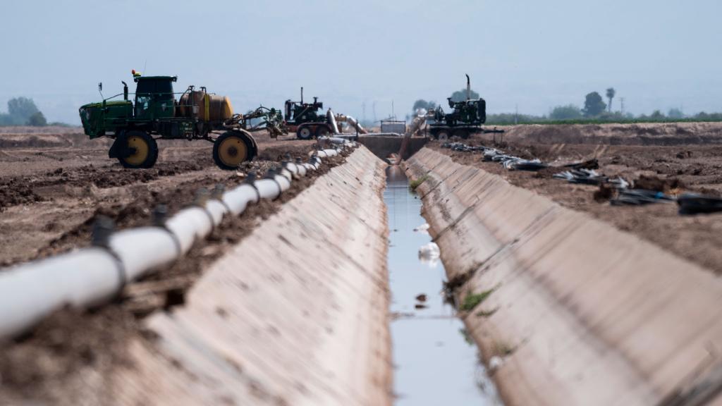 Low angle of an irrigation canal with farm equipment on either side, and drought-ridden land